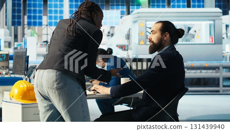 Man in photovoltaics factory talking with woman, diagnosing malfunctioning systems. Solar panels manufacturing plant manager receiving feedback from african american worker working to reduce downtime 131439940
