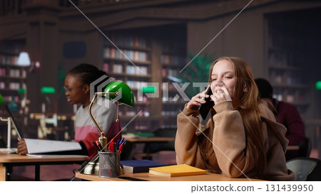 Noisy girl disturbing students at the library by speaking very loud on call, being rude and answering her phone in the study area. Disruptive annoying person asked to keep silence. Camera A. Noisy girl disturbing students at the library by speaking very loud on call, being rude and answering her phone in the study area. Disruptive annoying person asked to keep silence. Camera A. 131439950