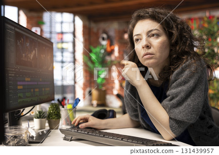 Video creator woman editing a music video on dual monitors in agency studio, multitasking between timeline editing and color grading. Professional editor uses tech tools and software. Video creator woman editing a music video on dual monitors in agency studio, multitasking between timeline editing and color grading. Professional editor uses tech tools and software. 131439957