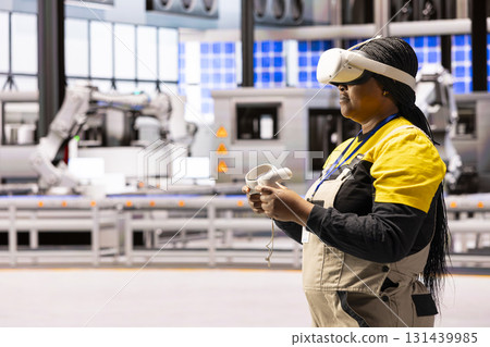 Automation engineer integrates virtual reality into manufacturing process at smart factory. Black female industry 4.0 worker uses VR headset and controllers to enhance training and troubleshooting. 131439985