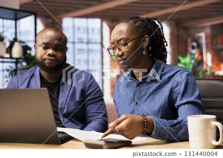 Black couple managing their self employed business finances and taxes, tracking expenses and income while they work remotely from their loft. Doing tax calculations for a debt free year. Black couple managing their self employed business finances and taxes, tracking expenses and income while they work remotely from their loft. Doing tax calculations for a debt free year. 131440004