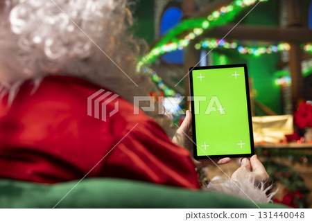 Santa Claus reads mockup tablet display to check naughty and nice kids list. Entertainer playing xmas character analyzes children behavior, preparing gifts for good children using green screen device Santa Claus reads mockup tablet display to check naughty and nice kids list. Entertainer playing xmas character analyzes children behavior, preparing gifts for good children using green screen device 131440048