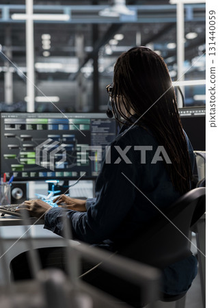 Data center call center agent providing logistics support to businesses, talking in headset mic. Worker in server room establishment overseeing node trees and communicating with engineers 131440059