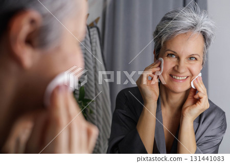 Mature well-groomed beautiful woman during menopause with grey hair removes daytime makeup Mature well-groomed beautiful woman during menopause with grey hair removes daytime makeup 131441083