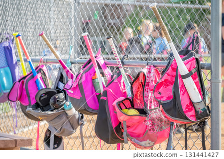 Brightly colored softball bags hang on a chain link fence at a sports field during a practice session in the afternoon sunlight 131441427