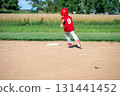 Young boy in red jersey runs towards first base during a sunny baseball game in a rural field 131441452
