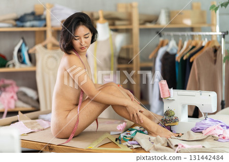 Nude woman posing sitting on table in sewing workshop 131442484