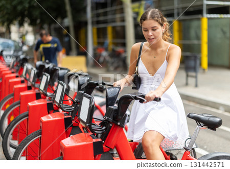 Young girl taking red bicycle from Bicing rental station 131442571