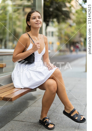 Positive young girl sitting at bus stop Positive young girl sitting at bus stop 131442625