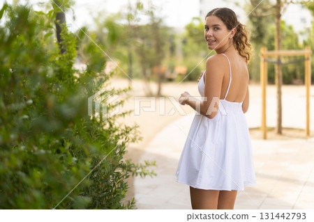 Young girl in white summer dress walking in park 131442793
