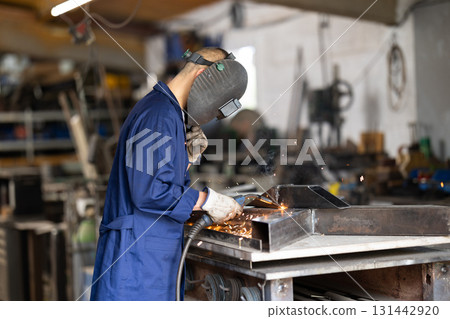 Male welder standing with a welding semi-automatic machine and a safety helmet in metal machining workshop 131442920
