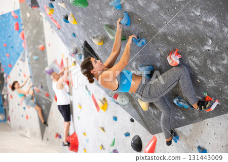 Young girl climbing on artificial rock wall in rock-climbing gym Young girl climbing on artificial rock wall in rock-climbing gym 131443009