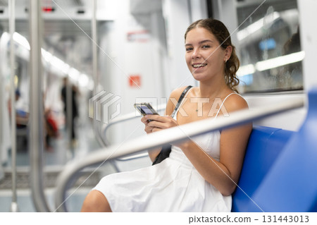 woman in a dress is sitting in a subway car with a phone in her hands 131443013
