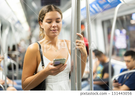 young woman stands in a subway car with a mobile phone in her hands 131443056
