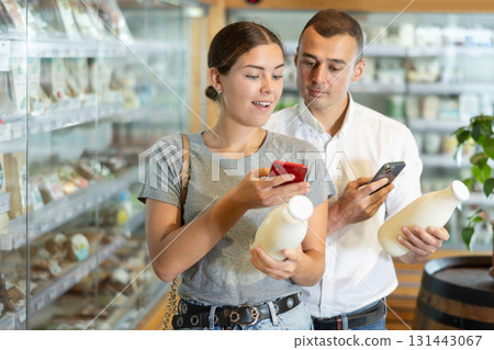 Positive young couple scanning QR code on milk bottle in large supermarket Positive young couple scanning QR code on milk bottle in large supermarket 131443067