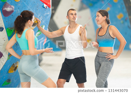 Athletic man and two sporty women discussing climbing options near climbing wall 131443070