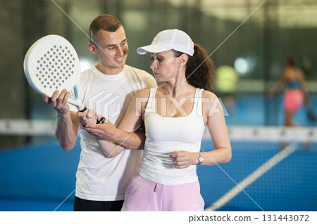 Male trainer teaches woman to play padel and hold racket correctly to hit ball 131443072