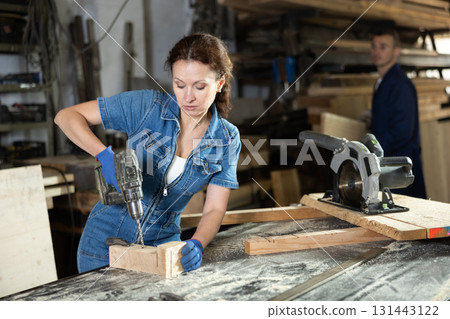Work in woodworking enterprise - woman drills a hole with drill 131443122