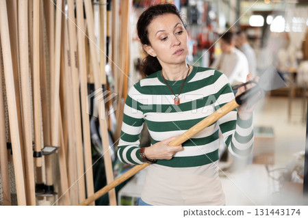 Woman carefully inspects garden hoe before purchasing it at hardware store Woman carefully inspects garden hoe before purchasing it at hardware store 131443174