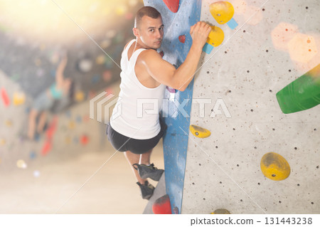 Atlete man grabbing ledges of artificial climbing wall in bouldering centre Atlete man grabbing ledges of artificial climbing wall in bouldering centre 131443238