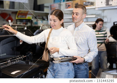 Young married couple chooses a new grill in supermarket for their yard Young married couple chooses a new grill in supermarket for their yard 131443295