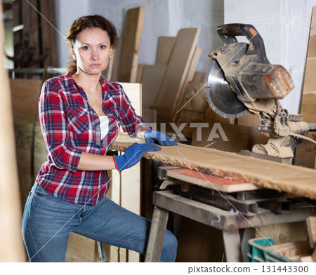 Working at sawmill - woman saws wooden board using circular saw 131443300