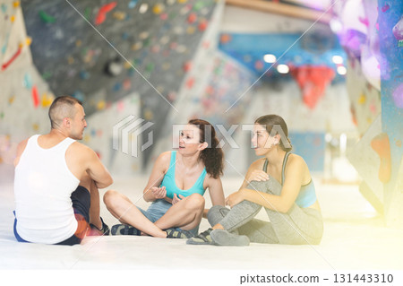 Young man and two women talking merrily sitting on floor in climbing hangar 131443310