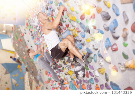 Sporty man in doing difficult wall climb in climbing gym without special climbing equipment Sporty man in doing difficult wall climb in climbing gym without special climbing equipment 131443339