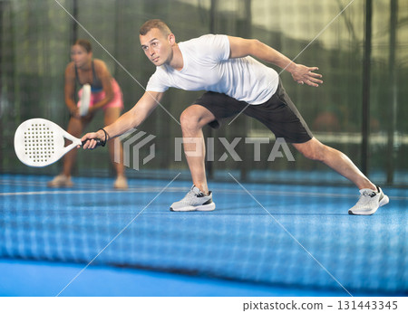 Male players playing padel in a padel court indoor behind net Male players playing padel in a padel court indoor behind net 131443345