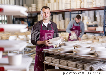 Artisan stacking crafted ceramic plates on racks in workshop 131443346