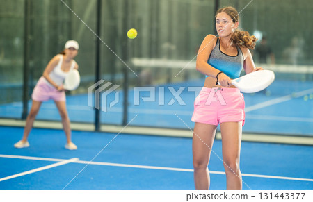 Sportive woman and other members engaged in Padel Tennis in indoor court of tennis club 131443377