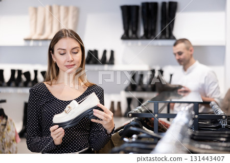 Girl buyer looks at footwear from new collection and picks up new pair of moccasins shoes Girl buyer looks at footwear from new collection and picks up new pair of moccasins shoes 131443407