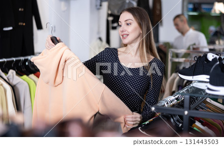 Woman stopped near clothing showcase, holds cardigan hanger in hands, examines product 131443503
