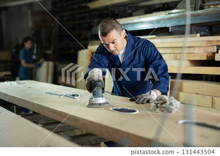 During manufacturing, man employee grinds surface of wooden board, gives smoothness to surface During manufacturing, man employee grinds surface of wooden board, gives smoothness to surface 131443504