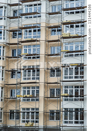Facade of new multistory building under construction. Scaffolding on residential house. 131444166