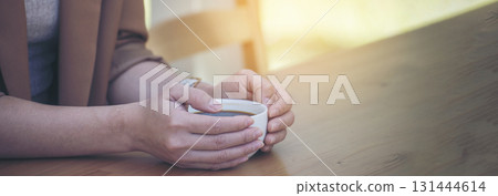Banner hands of woman sitting office desk holding sweet coffee cup relax and enjoy with happy time. Panorama Hot coffee mug. Woman holding coffee cup relaxing after work at office in cafe copy space Banner hands of woman sitting office desk holding sweet coffee cup relax and enjoy with happy time. Panorama Hot coffee mug. Woman holding coffee cup relaxing after work at office in cafe copy space 131444614