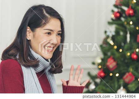 Asian Woman sitting christmas gift box under xmas tree got surprise present gift. Women smile talk sitting under decor bauble ball christmas tree xmas holiday winter festival celebrate in living room 131444904