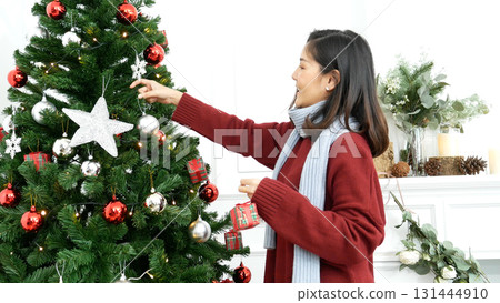 Woman hands decorate Christmas tree red ball, bauble, snow flake. Asian woman decor bauble ball christmas tree in xmas holiday winter seasonal celebration. Close up hands holding silver star decorate 131444910