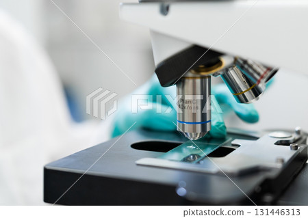 Scientist in laboratory closely examining specimen under microscope. 131446313