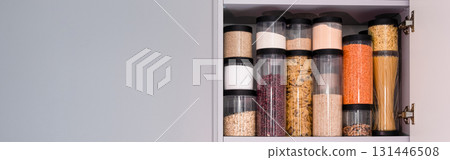 Organized kitchen pantry with cylindrical plastic jar for storing loose products, in grey tones. banner Organized kitchen pantry with cylindrical plastic jar for storing loose products, in grey tones. banner 131446508