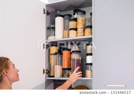Organized kitchen pantry with cylindrical plastic jar for storing loose products, in grey tones Organized kitchen pantry with cylindrical plastic jar for storing loose products, in grey tones 131446517