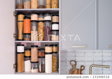 Organized kitchen pantry with cylindrical plastic jar for storing loose products, in grey tones 131446518