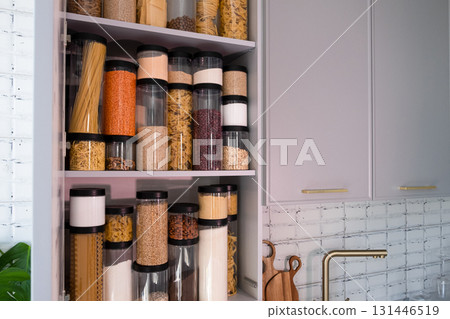 Organized kitchen pantry with cylindrical plastic jar for storing loose products, in grey tones Organized kitchen pantry with cylindrical plastic jar for storing loose products, in grey tones 131446519