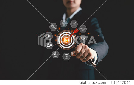 Businesswoman uses magnifying glass to focus on target board icon, symbolizing business concept of strategic planning, goal achievement, and innovation, key drivers of success in modern enterprises. 131447045