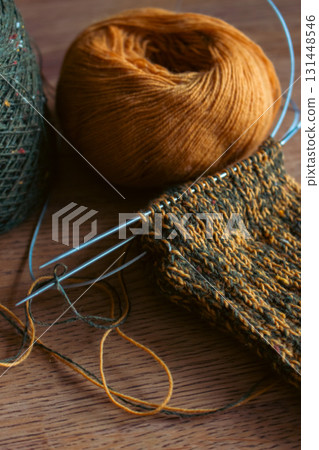 Cozy knitted socks with yarn ball and knitting needles. Knitting process of wool socks. Cozy autumn vibes. Yellow and green tweed yarn on wooden table. Knitting hobby. Knitwear concept. Cozy knitted socks with yarn ball and knitting needles. Knitting process of wool socks. Cozy autumn vibes. Yellow and green tweed yarn on wooden table. Knitting hobby. Knitwear concept. 131448546