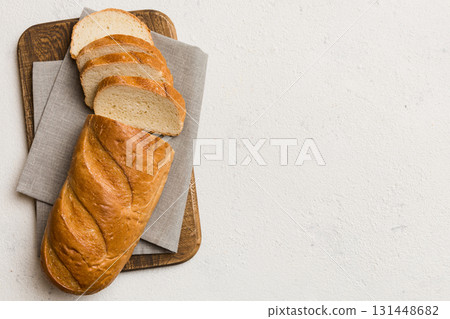 Freshly baked bread slices on cutting board against white wooden background. top view Sliced bread 131448682