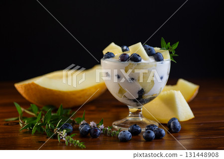 Delicate yogurt with juicy pieces of melon and fresh blueberries on a wooden Delicate yogurt with juicy pieces of melon and fresh blueberries on a wooden 131448908
