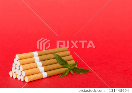 Menthol cigarettes and fresh mint leaves on colored background, Many cigarettes stacked together top view flat lay Menthol cigarettes and fresh mint leaves on colored background, Many cigarettes stacked together top view flat lay 131448994
