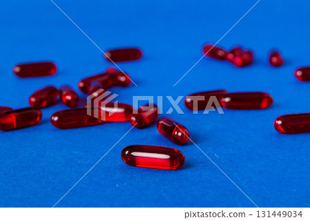 Heap of red pills on colored background. Tablets scattered on a table. Pile of red soft gelatin capsule. Vitamins and dietary supplements concept Heap of red pills on colored background. Tablets scattered on a table. Pile of red soft gelatin capsule. Vitamins and dietary supplements concept 131449034