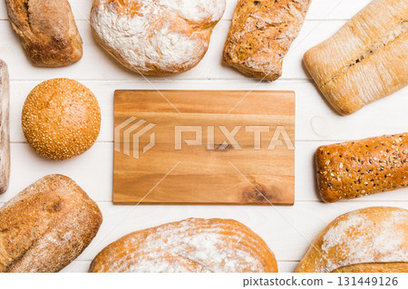 Minimalist wooden cutting board blank mockup on background of Types of homemade bread. Different kinds of fresh bread as background, top view with space for your text or design 131449126